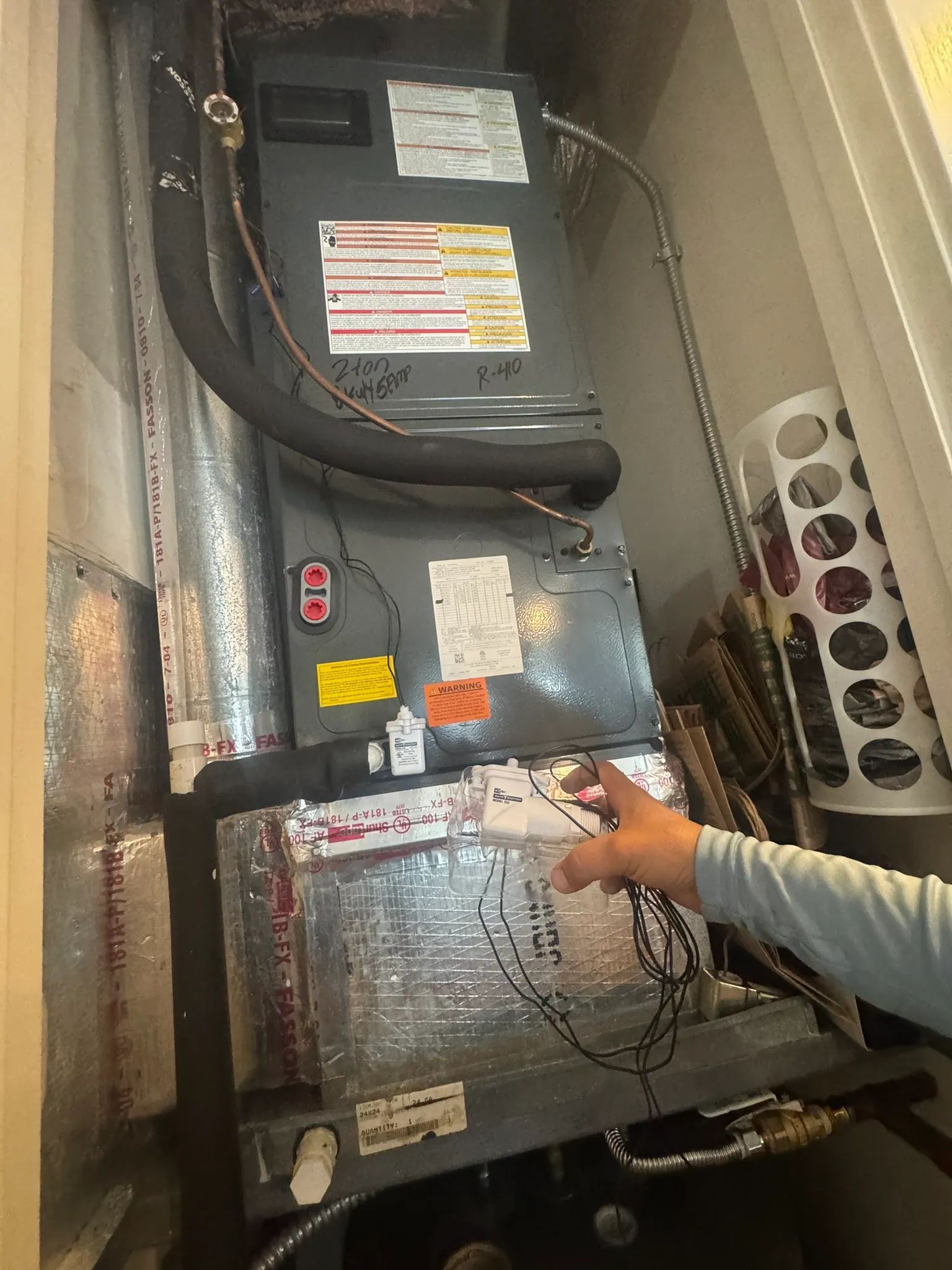 Technician holding a condensate float switch next to an air handler marked 2-ton R-410A