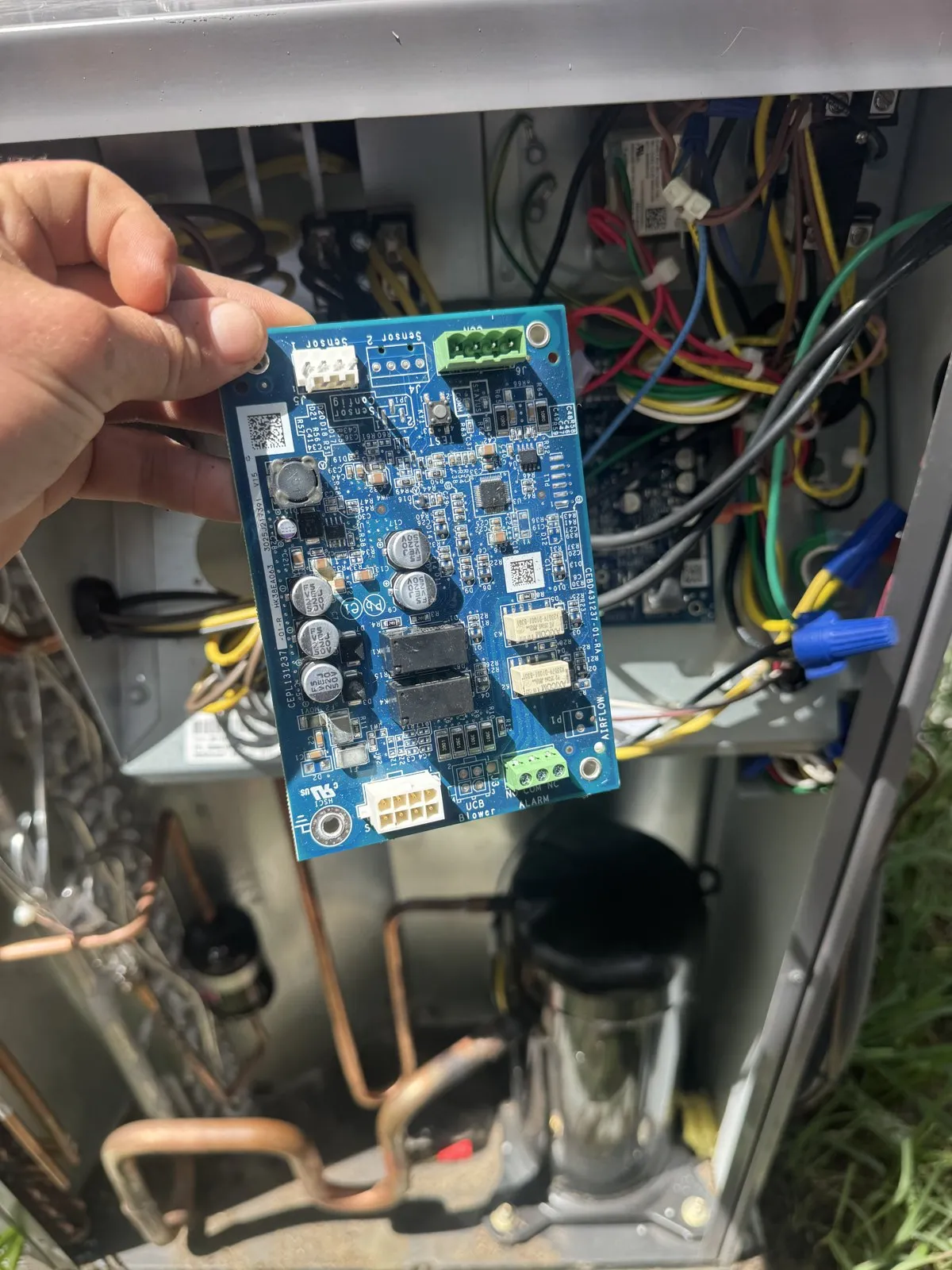 Technician holding an outdoor unit control board pulled for testing, north Pasco County FL